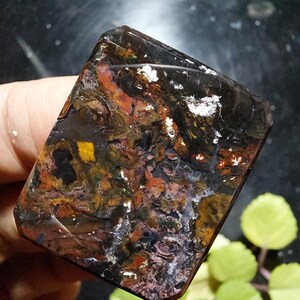 以下が含まれることがあります： 複雑な色のパターンを持つ、長方形の研磨された宝石。濃い茶色、黒、オレンジ、黄色、白の色合いが混ざり合い、ユニークで自然なデザインを作り出しています。エッジは滑らかで、表面は反射します。