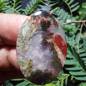 Op de afbeelding: Een gladde, ovale agaat met een uniek patroon van rood, wit, groen en bruin. De steen is doorschijnend en laat licht door.