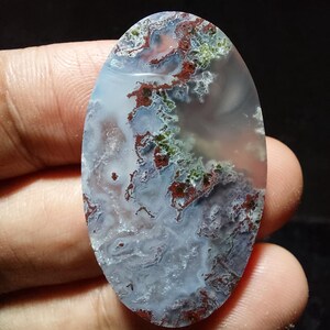 May include: An oval-shaped gemstone with a unique pattern. The stone features a blend of colors, including white, blue, red, and green, creating a marbled effect. The polished surface highlights the natural variations and textures within the stone.