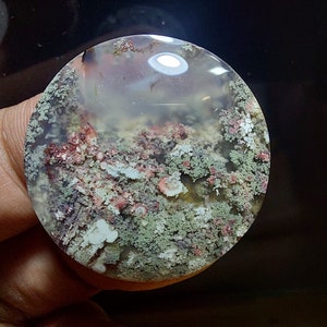 May include: A round, translucent agate cabochon with a unique, moss-like pattern in shades of green, pink, and white.