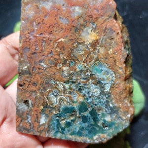 Może przedstawiać: Surowy kamień szlachetny z mieszanką kolorów. Kamień ma obszary głębokiego turkusu, rdzy i brązu, ze skomplikowanymi wzorami i teksturami. Cięcie ukazuje naturalny, surowy wygląd.