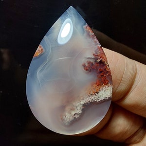 Peut inclure: Un cabochon d'agate en forme de larme avec un motif de couleur blanc, gris et brun. L'agate a une apparence translucide avec une surface lisse et polie.