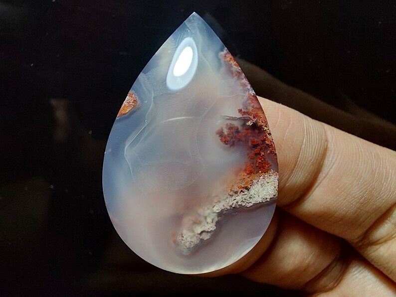 Peut inclure: Un cabochon d'agate en forme de larme avec un motif de couleur blanc, gris et brun. L'agate a une apparence translucide avec une surface lisse et polie.