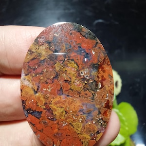 Peut inclure: Une pierre précieuse ovale aux couleurs vives. La pierre présente un mélange de rouge, d'orange, de jaune et des touches de bleu et de noir. La surface polie révèle un motif naturel et texturé, idéal pour les bijoux ou l'exposition.