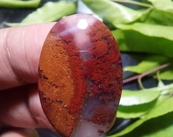 Könnte beinhalten: Ein glatter, ovaler Achat-Cabochon mit einem weißen Zentrum und roten und orangefarbenen Bändern. Der Stein hat eine polierte Oberfläche und ist ein natürlicher Edelstein.