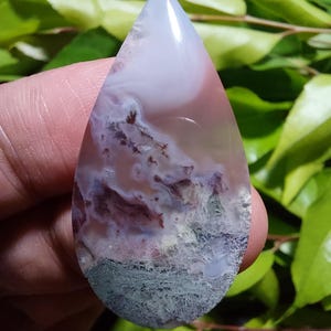 May include: A teardrop-shaped agate cabochon with a white, pink, and green color pattern. The agate has a cloudy, layered appearance with a smooth, polished surface.