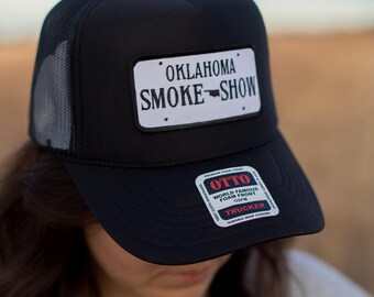 May include: Black trucker hat with a white patch that says "Oklahoma Smoke-Show". The hat also has a red and white patch that says "Otto World Famous Foam Front OSFM Trucker Durable Snap Closure".