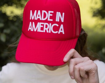 May include: Red trucker hat with white mesh back and the text "MADE IN AMERICA" in white lettering.