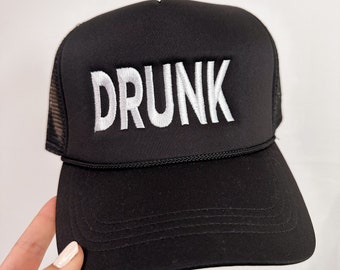 May include: Black trucker hat with a white embroidered word "DRUNK" on the front.