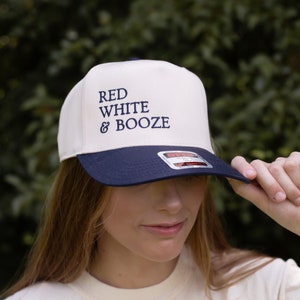 May include: A white and navy blue baseball cap with the text "RED WHITE & BOOZE" embroidered in navy blue on the front.