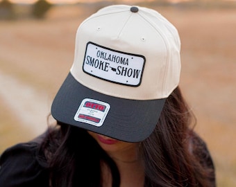 May include: A beige and black baseball cap with a black patch that says "Oklahoma Smoke Show" with a small outline of the state of Oklahoma.