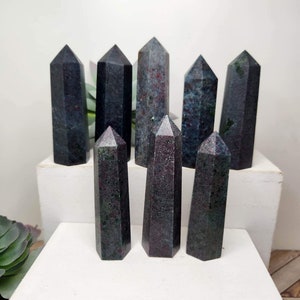 May include: Eight dark green and black gemstone points with red and white inclusions. The points are arranged in a staggered pattern on a white surface.
