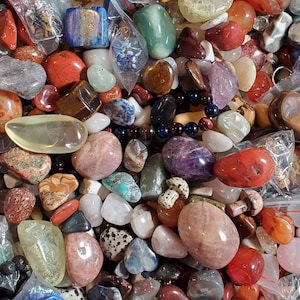 May include: A large collection of tumbled stones in various colors and shapes, including amethyst, rose quartz, tiger's eye, and clear quartz.
