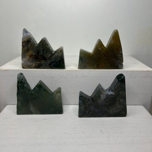 May include: Four green, gray, and white agate mountain sculptures. The sculptures are carved in the shape of a mountain range with three peaks.