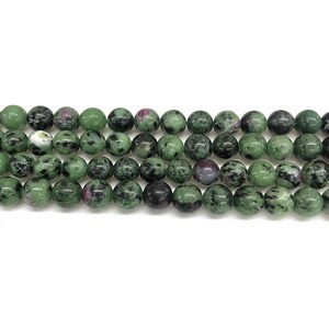 Puede incluir: Una hebra de cuentas de piedras preciosas verdes, negras y rosas. Las cuentas son redondas y tienen un aspecto moteado.