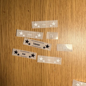 May include: A set of clear labels with black stars and white text. The labels are for various household items, including "Dyson", "Airer", "Extension", "Fan", "TV", "Sky".