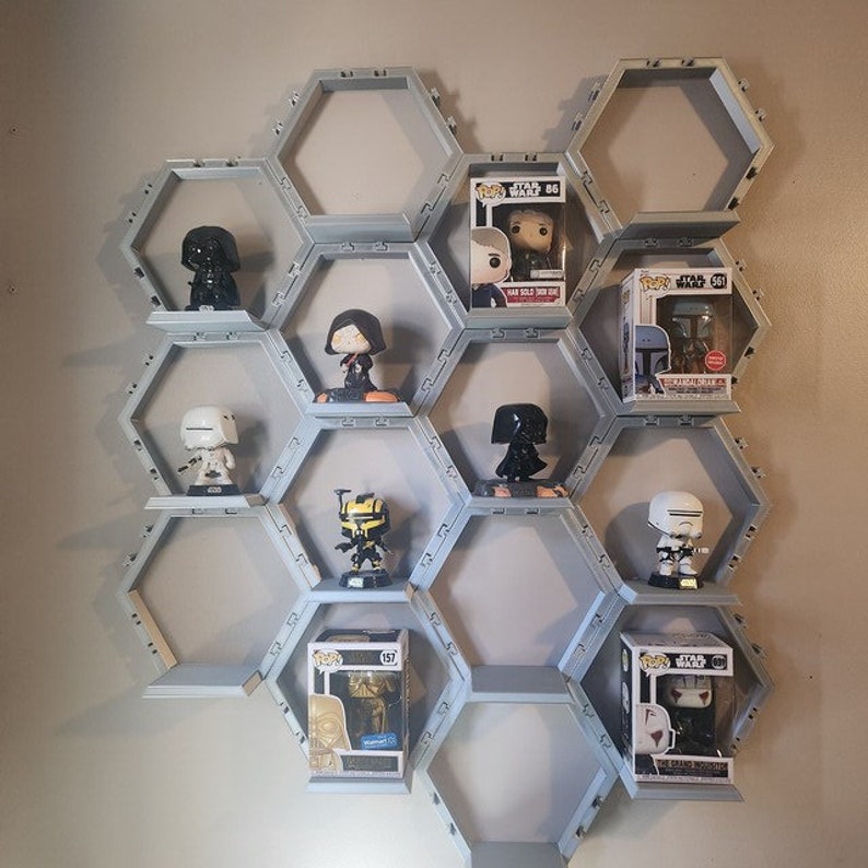 May include: A light gray modular honeycomb wall shelf system featuring multiple hexagonal compartments. The shelves hold various Star Wars Funko Pop figures, both loose and inside their original cardboard display boxes with clear plastic windows.