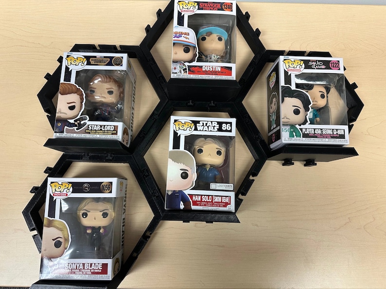 May include: Five Funko Pop vinyl figures in their original boxes, including Star-Lord, Dustin from Stranger Things, Player 456: Seong Gi-hun, Han Solo in snow gear, and Sonya Blade, all displayed on a black modular hexagonal wall-mounted shelf system.
