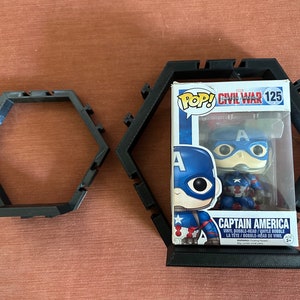 May include: Two black hexagonal display frames made of plastic, one empty and one containing a Captain America Funko Pop vinyl bobble-head figure in its original box, labeled Civil War 125, featuring the character in a blue and red suit.