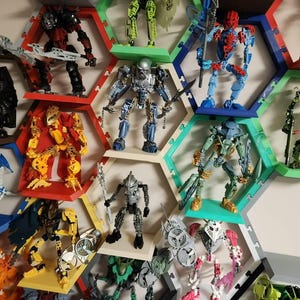 May include: A collection of Bionicle action figures displayed on a wall-mounted honeycomb shelving system. The figures feature various colors including red, blue, green, yellow, and silver, each posed on individual hexagonal shelves.