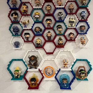 May include: A wall-mounted display system composed of interlocking hexagonal shelves in white, red, and teal. The shelves house a collection of various small vinyl character figurines, each positioned within its own individual hexagonal frame.