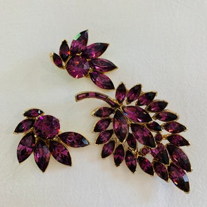 Könnte beinhalten: Ein Set aus drei Broschen in Blattform mit violetten Strasssteinen. Die Broschen sind aus goldfarbenem Metall gefertigt und haben einen Vintage-Look.