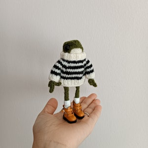 May include: A green knitted frog wearing a black and white striped sweater and brown boots.