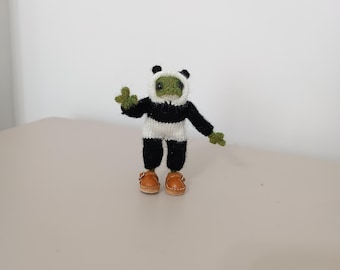 Puede incluir: Una pequeña rana de punto verde que lleva un disfraz de panda blanco y negro con zapatos marrones.