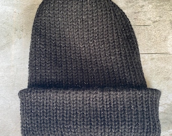 May include: A dark gray knit beanie with a folded brim. The hat has a ribbed texture and a subtle shimmer throughout the yarn. This winter hat is a warm and stylish accessory.