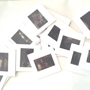 May include: A pile of white plastic slide frames with various images inside. The images are mostly dark and blurry.