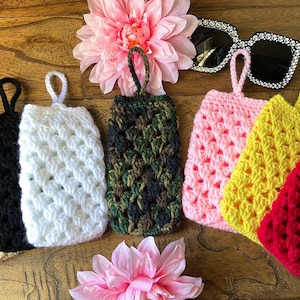 May include: Seven crocheted eyeglass cases in various colors, including beige, black, white, camouflage, pink, yellow, and red. The cases have a crocheted pattern and a loop for hanging.