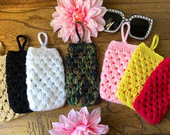 May include: Seven crocheted eyeglass cases in various colors, including beige, black, white, camouflage, pink, yellow, and red. The cases have a crocheted pattern and a loop for hanging.
