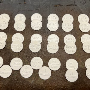 Może przedstawiać: Zestaw 20 białych plastikowych żetonów z różnymi napisami i symbolami. Żetony są używane do gier planszowych i zawierają modyfikatory do trafienia, ranienia, obrony, obrażeń i ponownego rzutu.