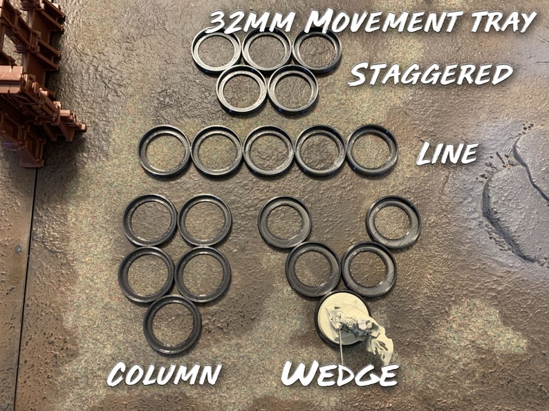 May include: A set of 32mm movement trays for tabletop games. The trays are arranged in different formations, including a line, a column, a wedge, and a staggered pattern. The trays are made of black plastic and have a smooth, circular shape.