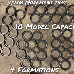 May include: A black plastic movement tray for miniature figures. The tray has 10 circular spaces for 32mm bases and can be used in 4 different formations. The tray is labelled "32MM MOVEMENT TRAY", "10 MODEL CAPACITY", and "4 FORMATIONS".