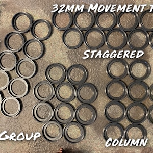 May include: A set of 32mm movement trays for tabletop games. The trays are arranged in four different patterns: line, staggered, group, and column. The trays are black and made of plastic.