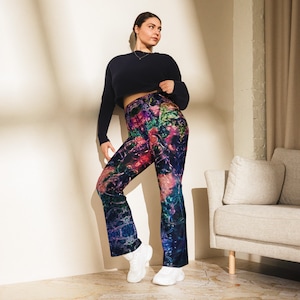 May include: A woman wearing a black cropped top and black and blue leggings with a colorful abstract print. The leggings have a flared leg.