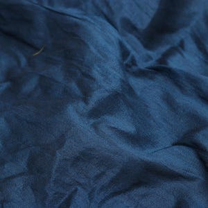 May include: A close-up of a deep blue fabric with a smooth, silky texture. The fabric is folded and draped, creating soft, flowing lines.