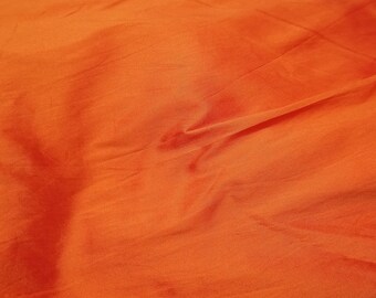 May include: Close-up of a bright orange fabric with a smooth texture. The fabric has a slight sheen and is folded in the center.