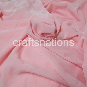 May include: A close-up of a soft, pink velvet fabric. The fabric is draped and folded, showing its texture and drape.