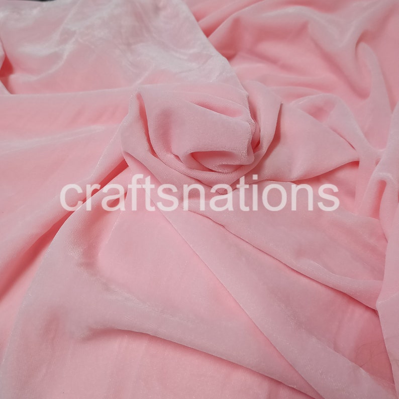 May include: A close-up of a soft, pink velvet fabric. The fabric is draped and folded, showing its texture and drape.
