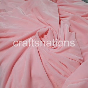 May include: A close-up of a soft, pink fabric with a smooth, silky texture. The fabric is draped and folded, creating a flowing, elegant look.