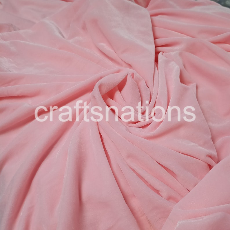 May include: A close-up of a soft, pink fabric with a smooth, silky texture. The fabric is draped and folded, creating a flowing, elegant look.