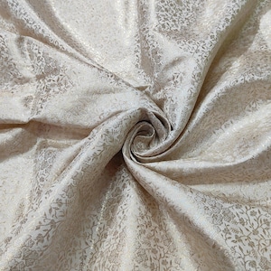 Pode incluir: Tecido creme com um padrão floral subtil e um ligeiro brilho. O tecido é reunido em espiral, mostrando a sua textura e caimento. O design apresenta delicados motivos florais repetidos num tom mais claro.
