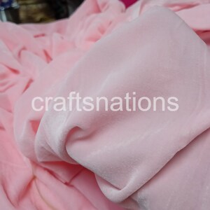 May include: Close-up of a soft, pink velvet fabric. The fabric is smooth and has a slight sheen. The fabric is folded and draped, showing its texture.
