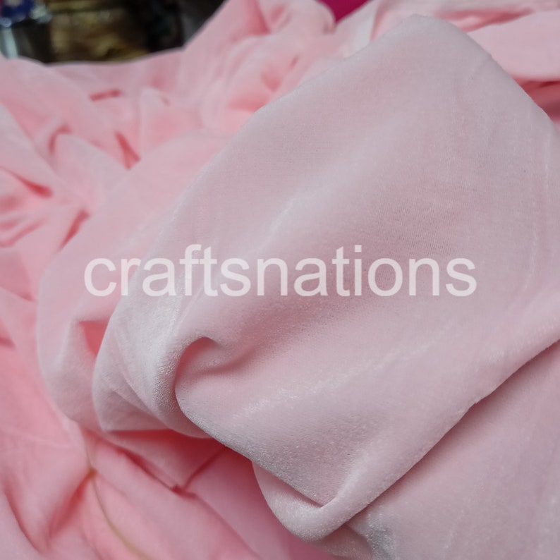 May include: Close-up of a soft, pink velvet fabric. The fabric is smooth and has a slight sheen. The fabric is folded and draped, showing its texture.
