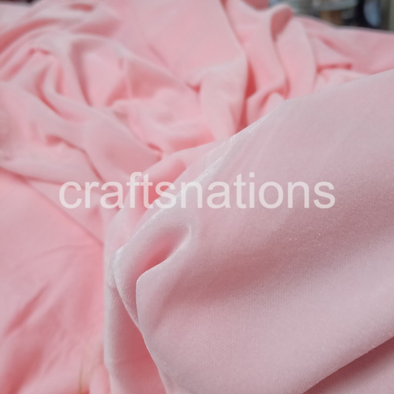 May include: A close-up of a soft, pink velvet fabric. The fabric is smooth and has a subtle sheen. The fabric is folded and draped, showing its texture and drape.