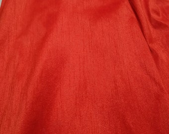 May include: A close-up of a smooth, red fabric with a subtle sheen. The fabric has a slightly textured surface, giving it a luxurious feel.