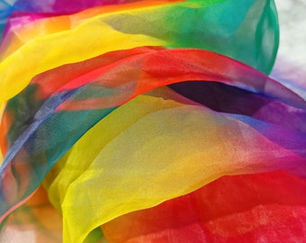 Op de afbeelding: Een veelkleurige stof in een regenboogspectrum, met lagen van doorschijnend materiaal. De kleuren zijn rood, oranje, geel, groen, blauw en paars. De stof is gerangschikt in vloeiende, overlappende plooien, waardoor een dynamische en kleurrijke weergave ontstaat.