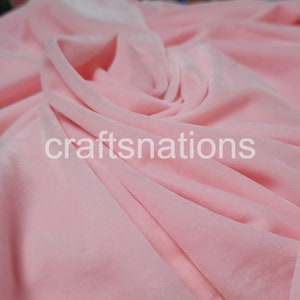 May include: A close-up of a soft, pink velvet fabric. The fabric is draped and folded, showing its texture and drape.